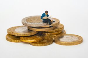 Miniature businessman sitting on top of a pile of coins, symbolizing MCA business loans and startup capital growth